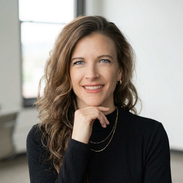 Amy Price, wearing a black top, smiling, in a bright office